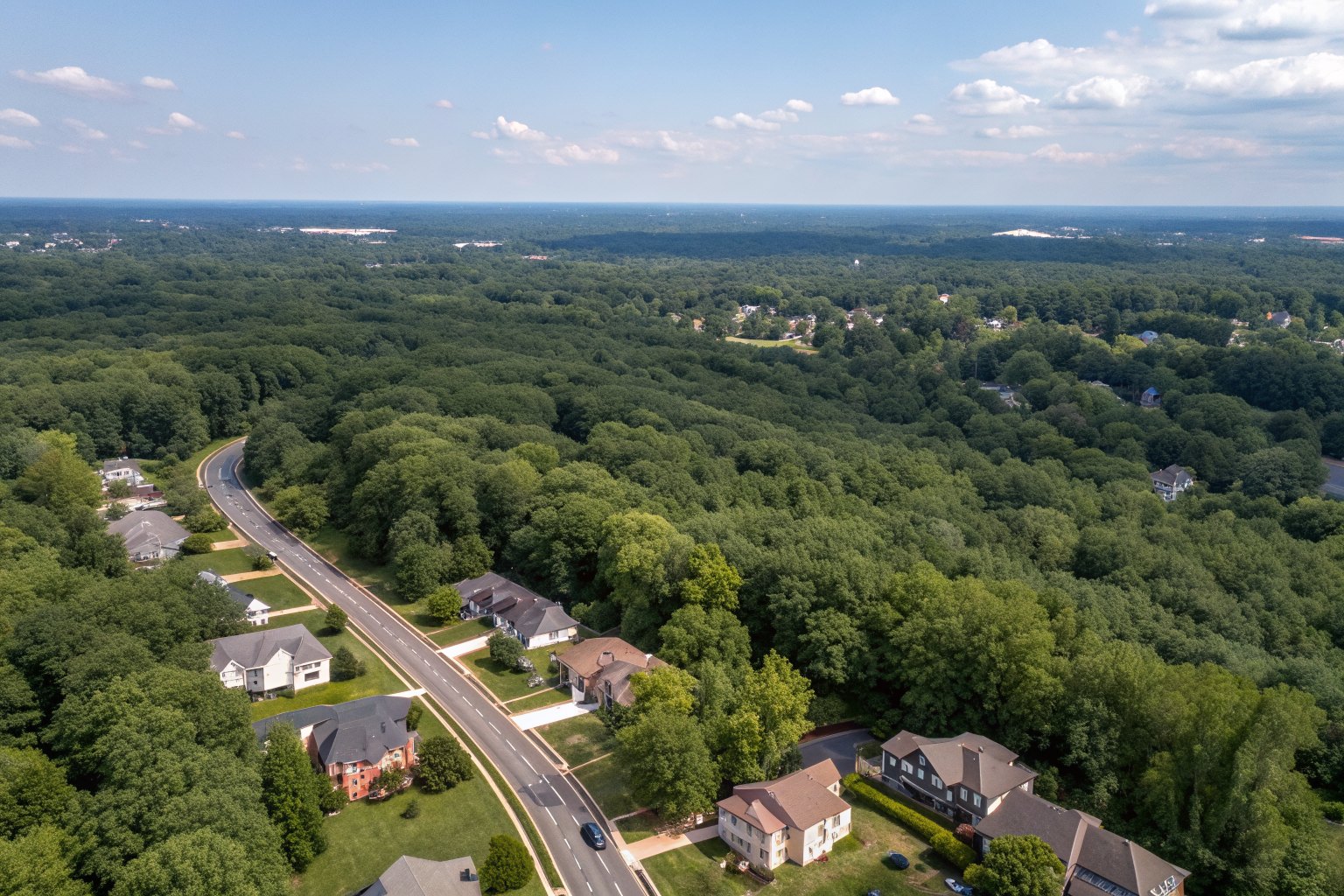 Aerial view of tree-covered suburbs with gray and brown shingle roofs and a highway curving through