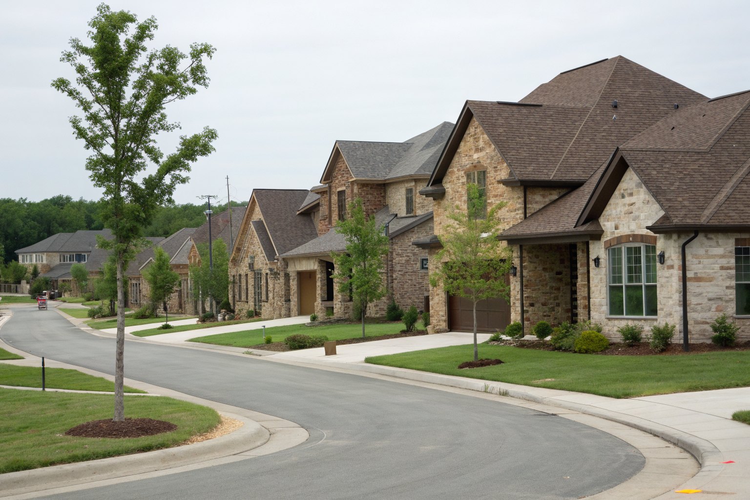 Newer two-story homes with stone fronts and brown architectural shingle roofs along a curving street