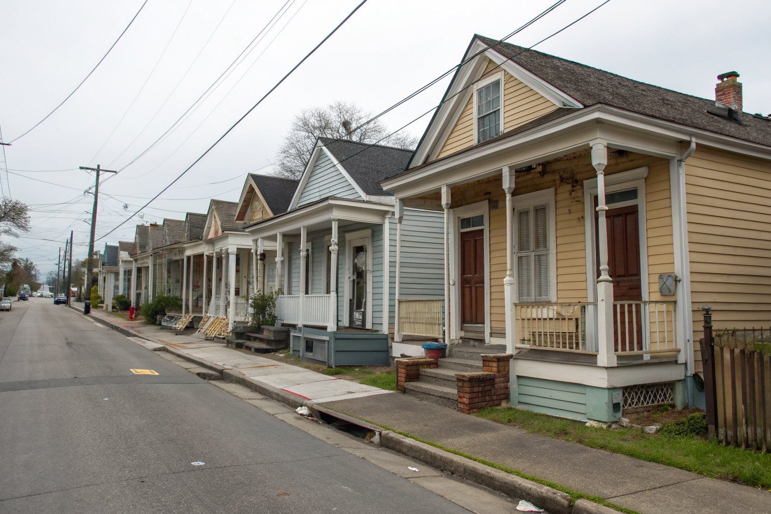 A row of narrow one-story shotgun houses with front porches and gable roofs